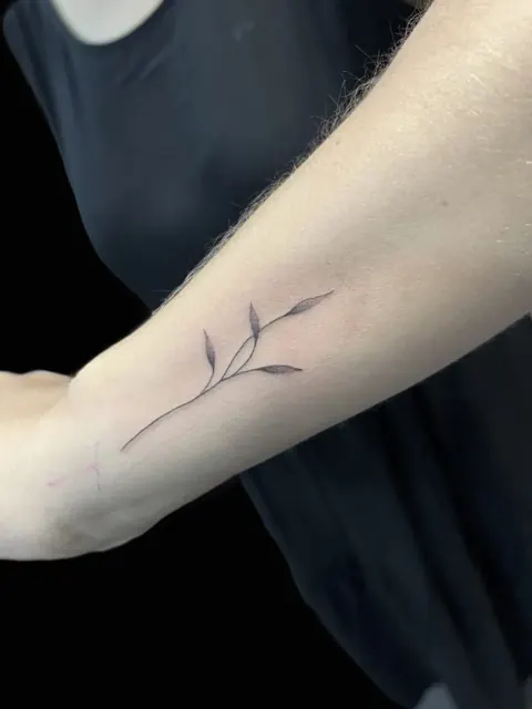 Tatouage fineline : fine branche feuillue sur le bras