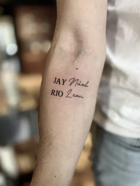 Fine inscription de prénoms en capitales et en cursive sur l’avant-bras