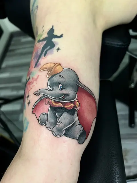 Farbiges Pop-Culture-Tattoo mit Dumbo und Peter-Pan-Silhouette am Arm