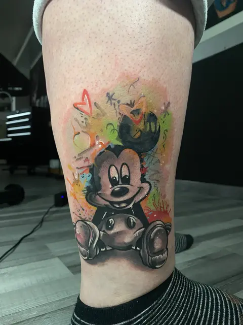 Pop-Culture-Tattoo mit Mickey Mouse auf buntem Aquarell-Hintergrund am Bein